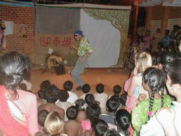 Bapoune dancing a jig before the newly built tea shop. At times the grey space at the background is transformed into a brightly lit window where the puppet show takes place.